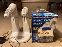 Photo showing the Arctic Air evaporative air cooler device, footwear dryer/sanitizer, and the product box with branding and product claims.