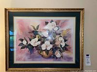 Framed floral print artwork featuring white flowers with pastel pink and purple background, hunter green matting, and gold frame