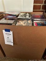 Photo of a large box filled with numerous audio CDs in jewel cases stacked and arranged loosely.