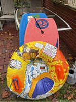 Photo showing the pink and blue boogie boards stacked with a colorful yellow-orange inflatable tube with cartoon characters and orange handles on top.