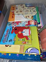 Photo of children's books stacked inside a plastic bin showing titles including Clifford's Birthday Treasure and a Texas-themed book.