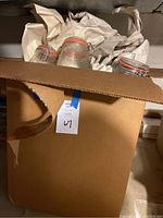 Box containing three clear glass Mason jars with orange rubber seals and metal clamp lids, partially wrapped in packing paper.