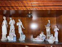 Full shelf view of eight Lladro figurines in wood cabinet