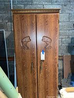 Front view of full height cabinet showing carved fish motifs and woodgrain finish