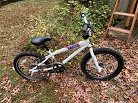Full side view of the youth bicycle showing white frame with branding, black tires, and saddle.