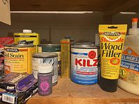 Photo of three wooden shelves filled with various home improvement liquids, wood fillers, stains, glues, and small cans shown from the front side.