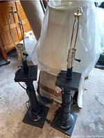 Two dark antique bronze finish table lamps, each with square stepped bases and bulbs holders with harp frames for lamp shades, cords visible wrapped around base
