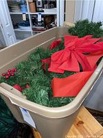 Plastic bin containing artificial evergreen garland with attached red fabric bows, red berry clusters, and other Christmas decorative elements.