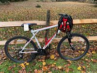 Full side view of white and red Palomar mountain bike leaning against fence with attached helmet on handlebars