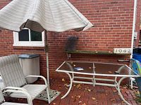 Full view of the glass top table with umbrella and chair showing condition and setting.