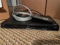 Philips DVD player on carpet with remote and coiled grey cable on top.