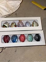 Two boxes containing ten decorative Polish pottery Easter eggs with intricate floral and folk art designs in multiple colors.