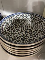 Stack of eight handmade Polish stoneware plates with detailed blue and white pattern showing floral motifs.
