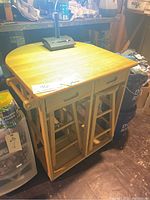 Front view of solid wood work bench with two stools tucked underneath and some items on top.