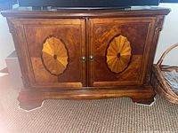 Front view of cherry veneer TV stand with decorative inlaid starburst panels on doors and round knobs.