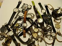 Full view of multiple watches including leather and metal band wristwatches, some with round faces, some gold tone, some silver tone.