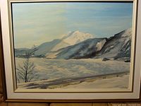 Full view of the framed winter landscape painting showing snow, mountains, and a tree with a light blue sky.