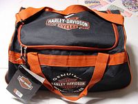 Photo showing the front of the Harley-Davidson black and orange duffel tote bag with logo and attached original tag.