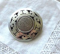 Top view of the round sterling silver brooch pendant with detailed Aztec calendar in the center and cut-out geometric border.