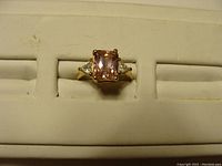 Front view of the 10k gold ring with pink center stone and simulated diamond side stones showing the setting and band.