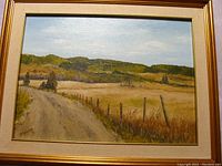 Framed oil on canvas landscape painting showing rural dirt road, fence, and hills.