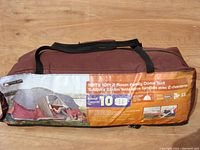 Photo of brown carry bag with Ozark Trail tent label showing dimensions 18ft x 10ft, two-room family dome design, sleeps 10, and other product features.