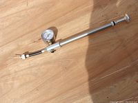 Full view of the bicycle air pump showing the metal body, pressure gauge, flexible hose, and valve connector.