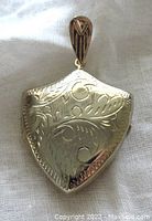 Front side of the shield-shaped locket pendant showing detailed floral and swirl engravings with a fancy bail.