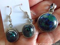 Photo showing the sterling silver pendant with round Lapis Lazuli gemstone held in hand with earrings featuring oval Malachite stones on card.