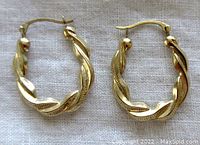 Pair of small twisted 10K yellow gold hoop earrings laid on white fabric, showing front view of both hoops