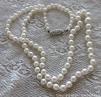 Full-length view of pearl necklace laid on lace, showing graduated bead sizes and overall condition