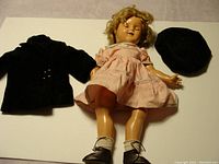 Full doll with pink dress, black jacket, black hat on a white background.