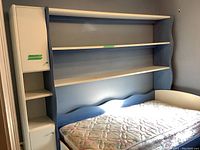 Twin bed frame with attached shelving unit showing three shelves and two cupboards, mattress on bed.