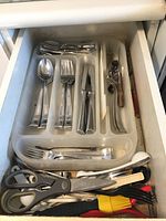Drawer organizer containing stainless steel spoons, forks, knives, plus kitchen scissors and other utensils including a pastry brush and another multi-tool.