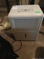 Full view of Mainstays dehumidifier from front, showing air vent, water level indicator, power cord on floor.