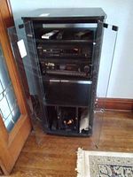 Full view of black wooden rack cabinet with glass doors housing Sony audio/video control equipment and accessories.