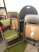 Two green upholstered seat metal folding chairs and one beige metal folding chair without upholstery on backrest