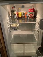 Interior view of refrigerator showing two glass shelves, bottom crisper drawers, and a few condiment bottles and drink cans inside.