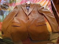 Front view of camel color Harry Rosen cashmere men's jacket with two-button closure and three front pockets laid flat on bed.