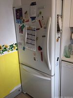 Full front view of white KitchenAid refrigerator with freezer drawer below, showing magnets and notes attached to the door.
