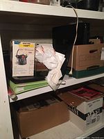 Box containing binders, a boxed corded headset, and some other office materials on a basement shelf