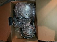 Box showing stainless steel pots and pans wrapped in clear plastic with visible black handles. Items show signs of heavy use and wear.