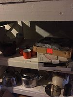 Shelving area showing teapot, kettle, orange mugs, boxed and bubble-wrapped Seder set, and various metal utensils on tray.