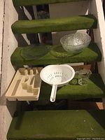 Clear glass bowls, white plastic colander, plastic organizer tray, and clear glass strainer placed on green-carpeted stairs.