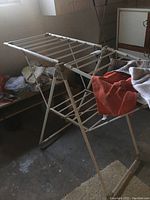 White plastic and metal drying rack with multiple horizontal bars, folded partially for storage in basement with some cloth on it.