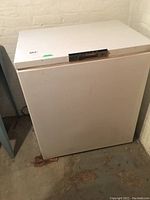 White rectangular chest freezer with top lid, located in basement on concrete floor.