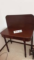 View of antique wooden table with folding hinged top and backboard, showcasing the smooth polished surface and shape.