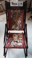 Front view of antique wooden folding rocking chair, showing floral needlepoint seat and back.