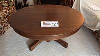Top view showing the round tabletop with oak grain and smooth finish, centered lot number card visible.