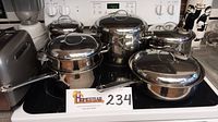 Five stainless steel pots with lids arranged on stovetop: large stockpot, medium stockpot, chicken fryer, double boiler and double steamer.